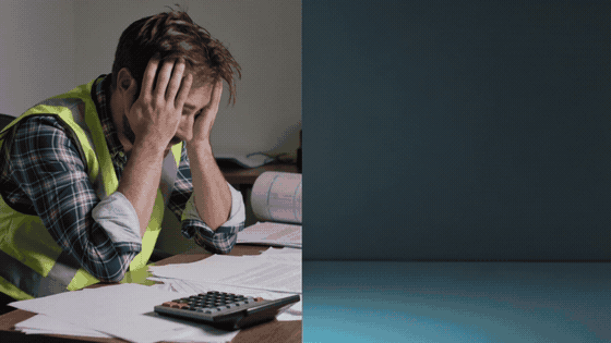 Stressed builder holding head in hands over paperwork and calculator — the late-night reality of manual renovation quoting